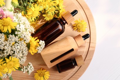 Glass bottles of essential oil and different wildflowers on white wooden table, top view