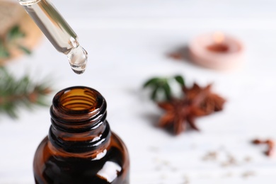 Photo of Dropping anise essential oil from pipette into bottle on table, closeup. Space for text