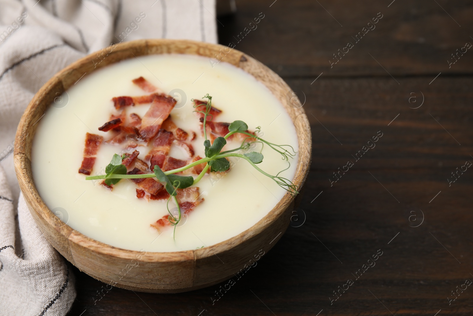 Photo of Delicious potato soup with bacon and microgreens in bowl on wooden table, closeup. Space for text