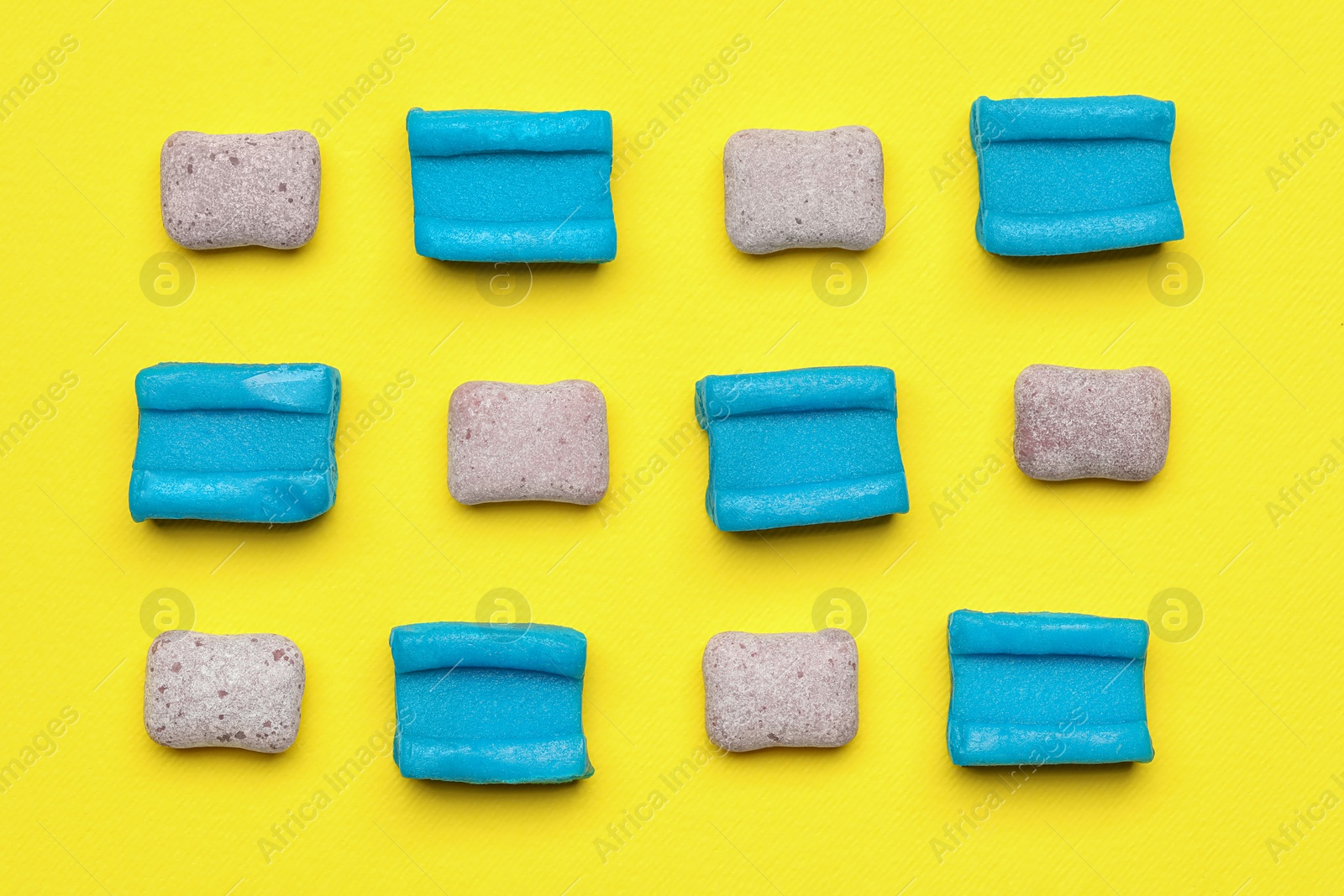 Photo of Different bubble gums on yellow background, flat lay