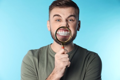 Young man with healthy teeth and magnifier on color background