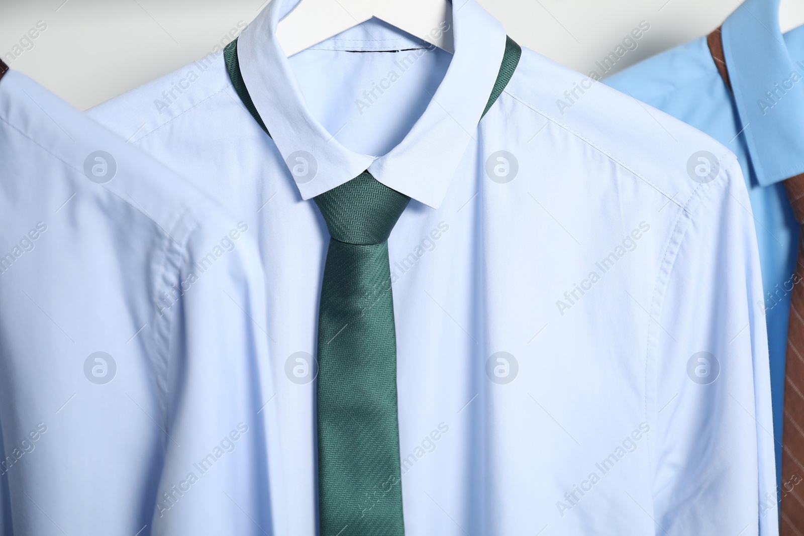 Photo of Hangers with shirts and neckties on light background, closeup