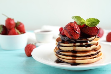Photo of Delicious pancakes with fresh strawberries and chocolate syrup on light blue wooden table