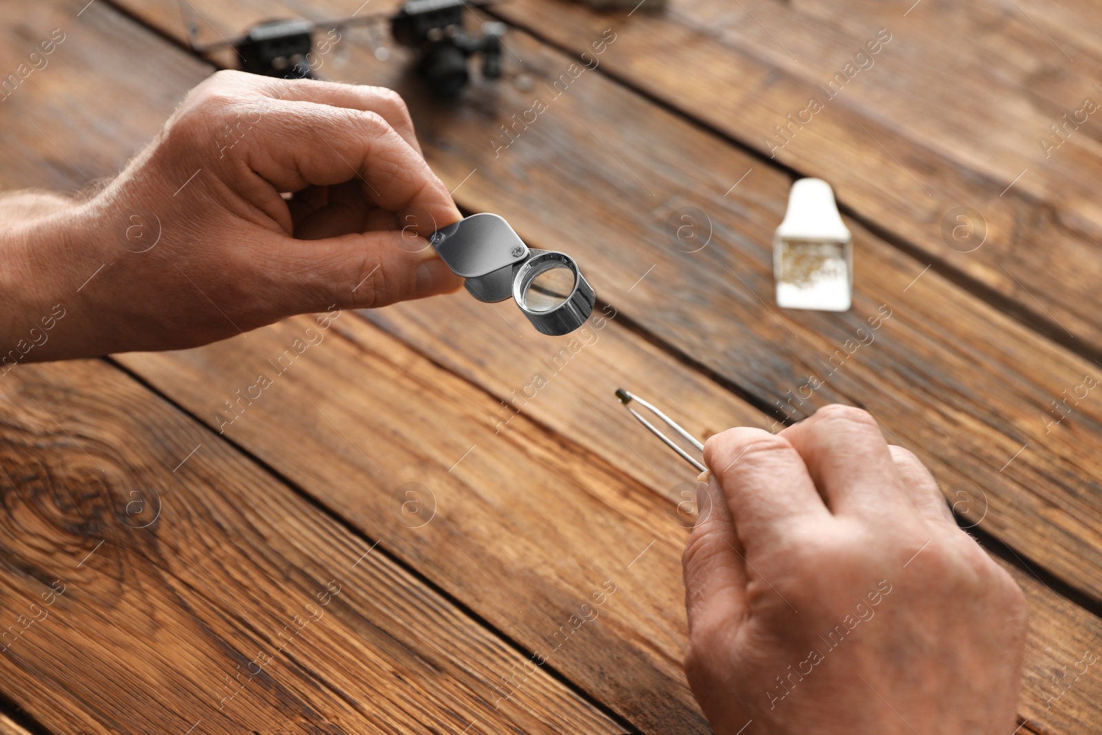 Photo of Male jeweler evaluating precious gemstone at table in workshop, closeup