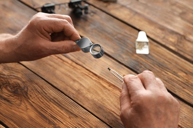 Male jeweler evaluating precious gemstone at table in workshop, closeup