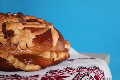 Photo of Rushnyk with korovai on light blue background, closeup. Ukrainian bread and salt welcoming tradition