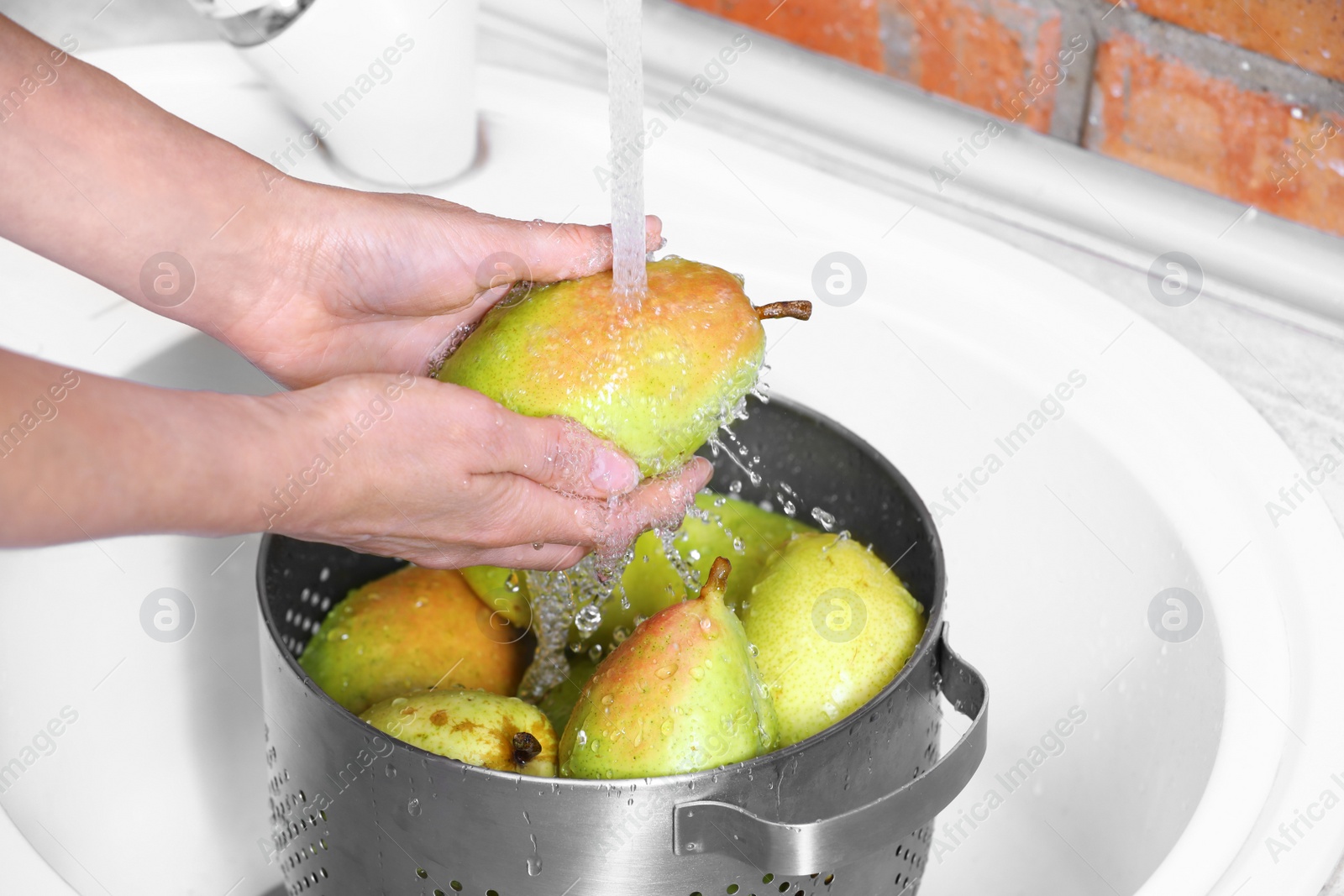 Photo of Woman washing fresh ripe pears in kitchen sink, closeup