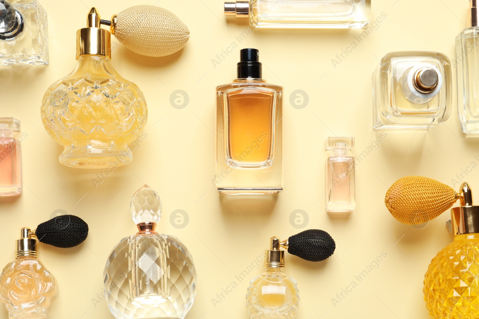 Photo of Flat lay composition with different perfume bottles on light yellow background