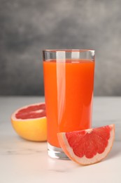 Photo of Tasty grapefruit juice in glass and fresh fruit on white table