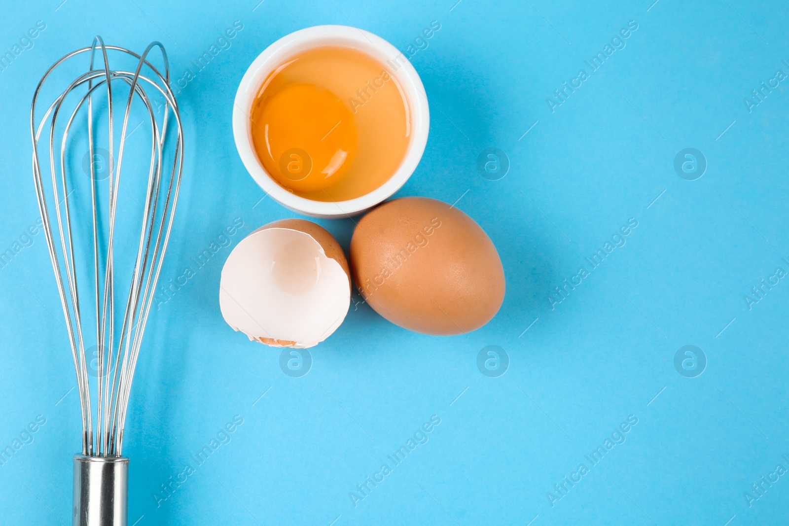 Photo of Raw eggs and whisk on light blue background,  top view with space for text. Baking pie