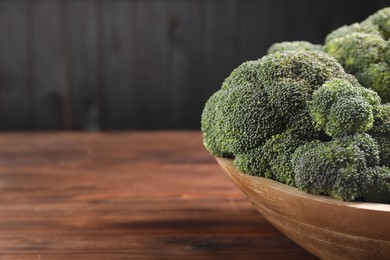 Bowl of fresh raw broccoli on wooden table, closeup. Space for text