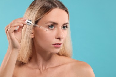 Photo of Beautiful woman applying cosmetic serum onto her face on light blue background, space for text