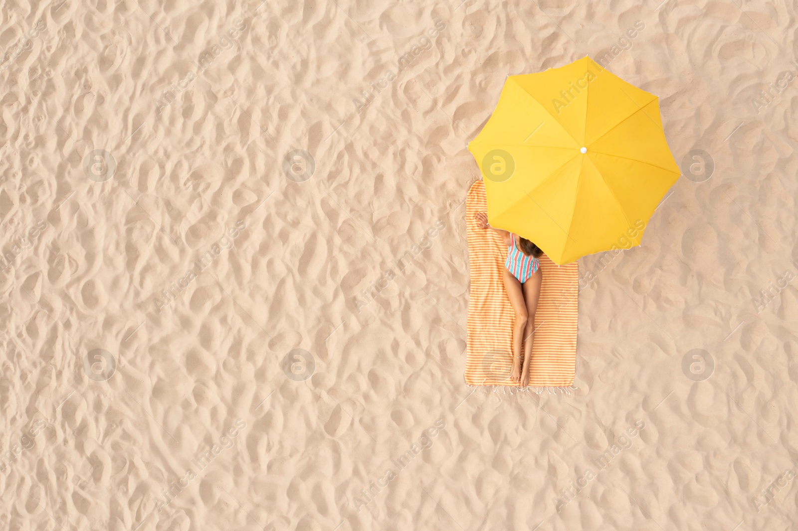 Image of Woman resting under yellow beach umbrella at sandy coast, aerial view. Space for text