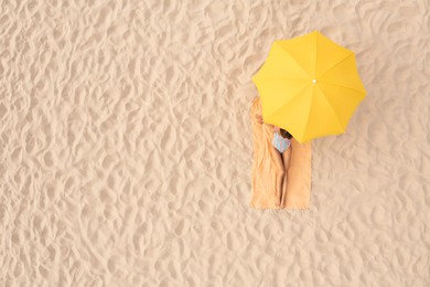 Image of Woman resting under yellow beach umbrella at sandy coast, aerial view. Space for text