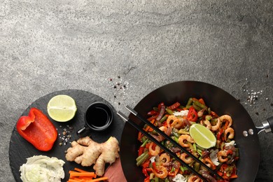 Photo of Shrimp stir fry with vegetables in wok and chopsticks on grey table, flat lay. Space for text