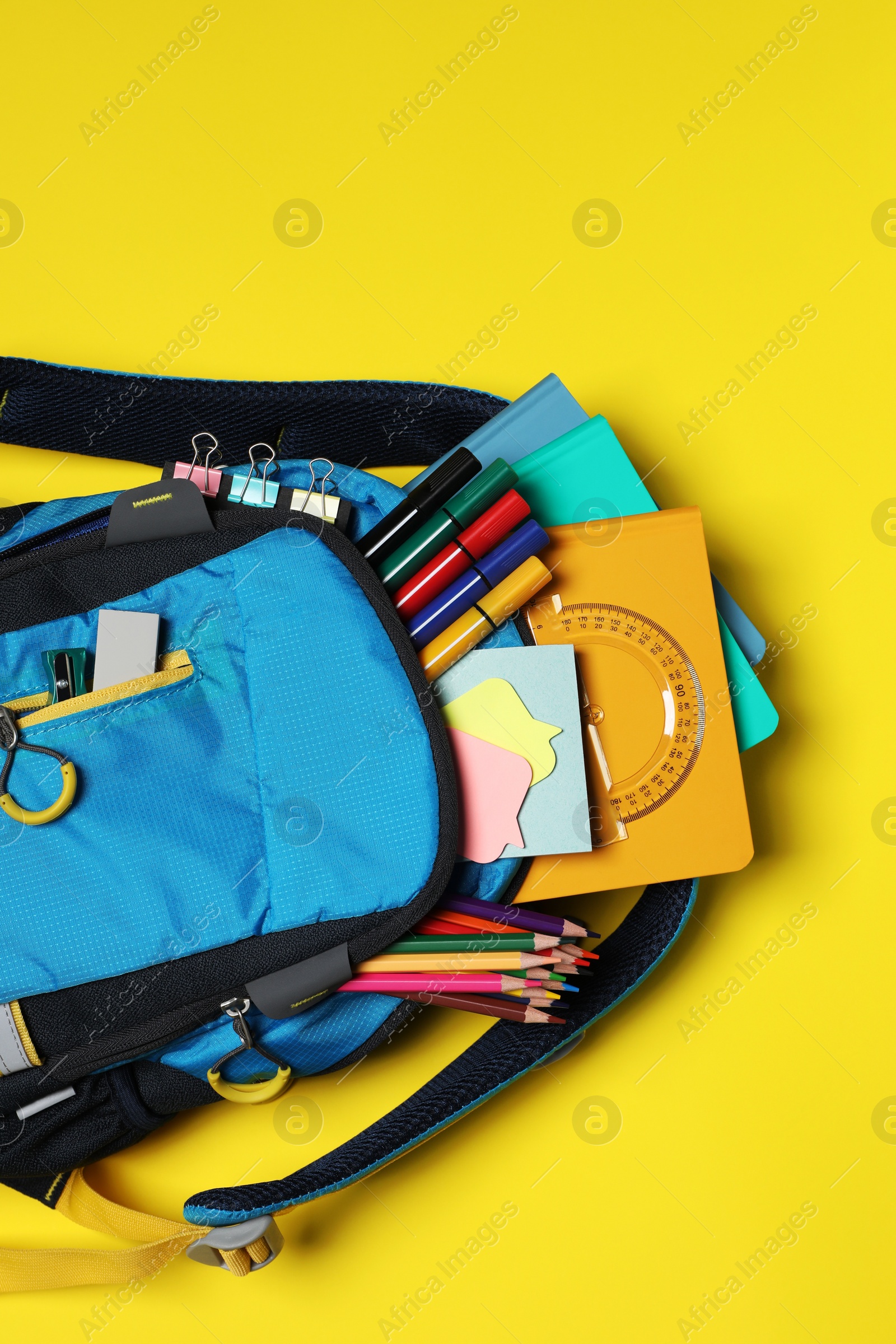 Photo of Backpack with school stationery on yellow background, top view. Space for text