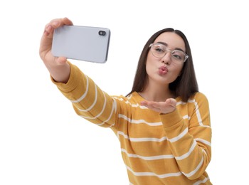 Young woman taking selfie with smartphone and blowing kiss on white background