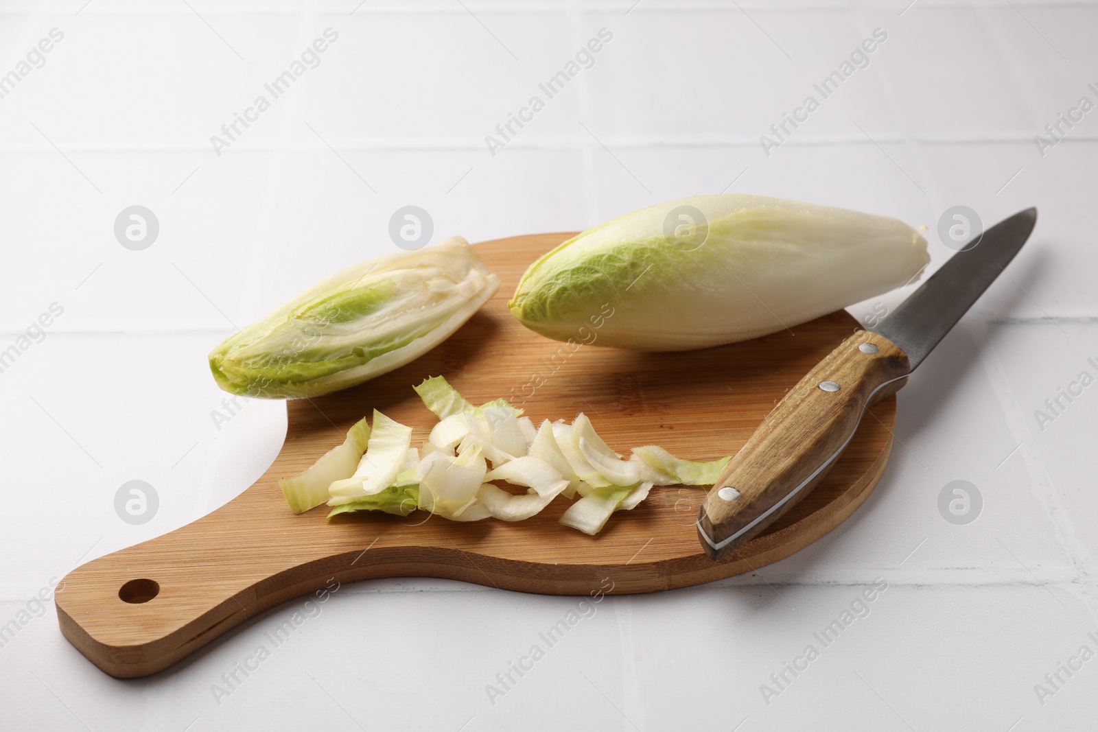 Photo of Fresh raw Belgian endives (chicory), wooden board and knife on white tiled table
