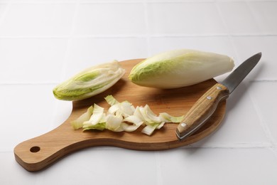 Photo of Fresh raw Belgian endives (chicory), wooden board and knife on white tiled table