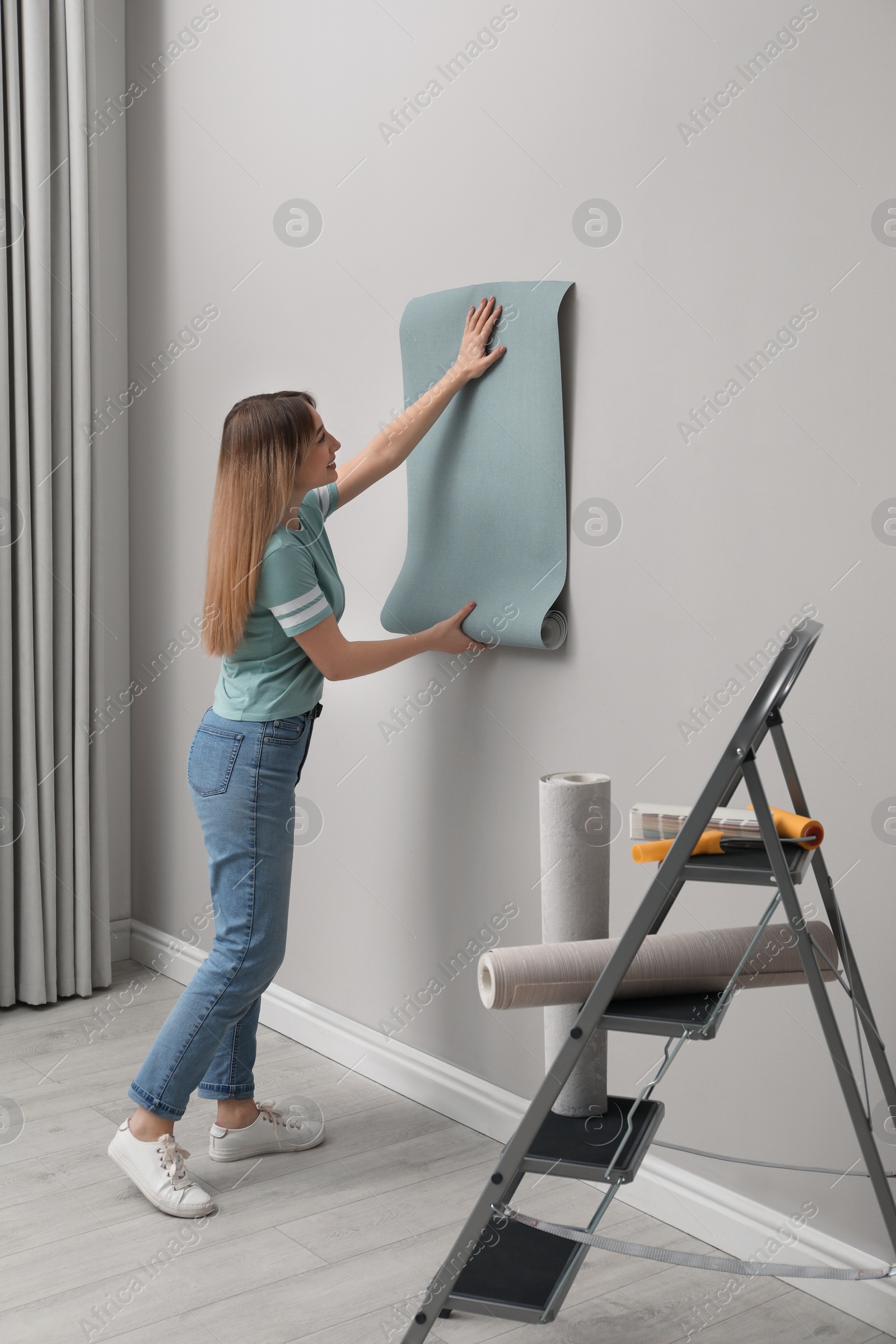 Photo of Woman hanging stylish wall paper sheet indoors