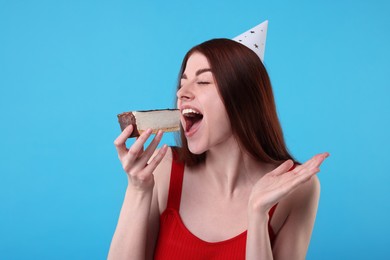 Photo of Young woman in party hat with piece of cake on light blue background
