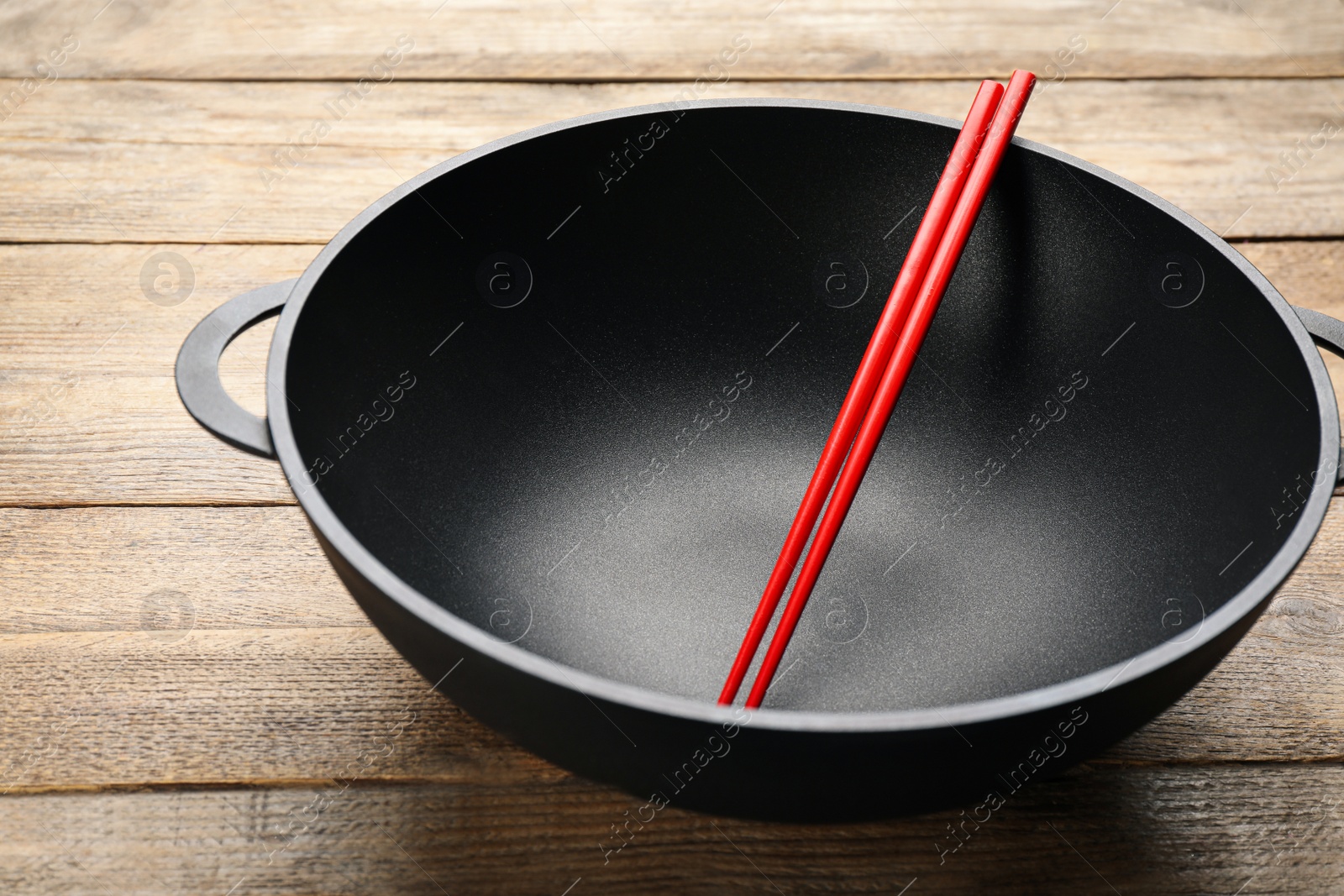 Photo of Empty iron wok with chopsticks on wooden table