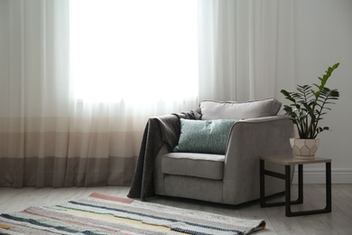 Cozy armchair with pillows and plaid near window in room. Interior design