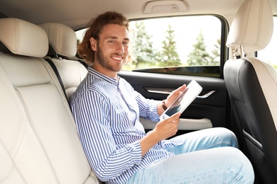 Photo of Attractive young man with tablet on backseat in luxury car