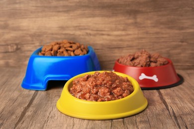 Dry and wet pet food in feeding bowls on wooden floor