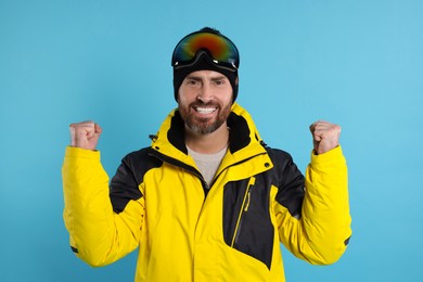 Photo of Winter sports. Cheerful man in ski suit and goggles on light blue background