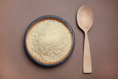 Photo of Parboiled rice in wooden bowl and spoon on color background, top view