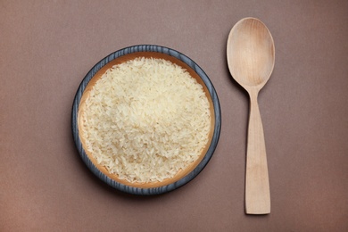 Parboiled rice in wooden bowl and spoon on color background, top view