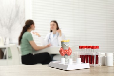 Photo of Endocrinologist examining patient at clinic, focus on model of thyroid gland and blood samples in test tubes