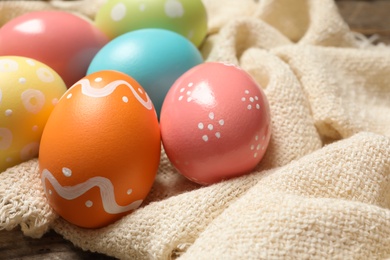 Photo of Colorful painted Easter eggs and cloth on table, closeup