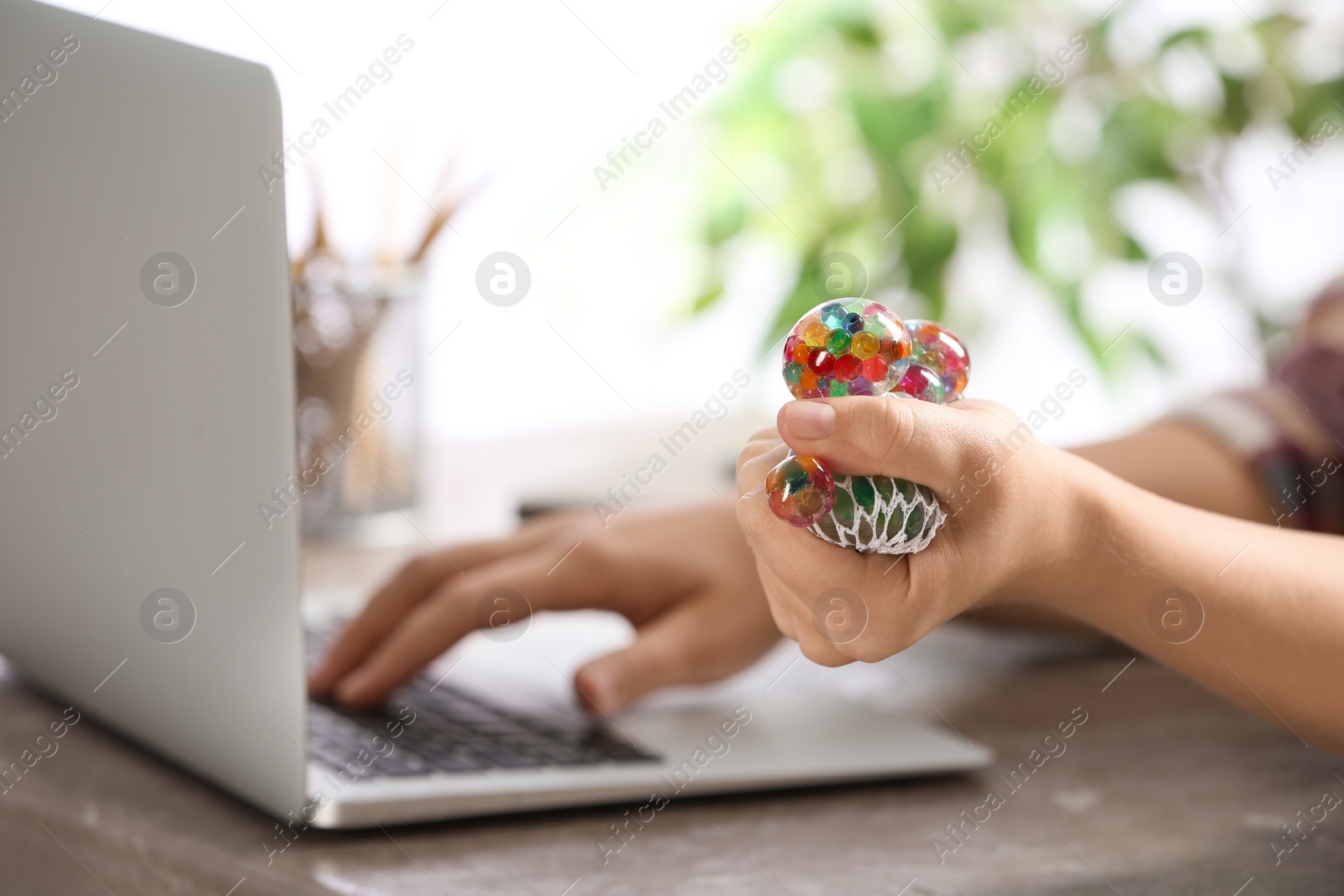 Photo of Woman squeezing colorful slime in office, closeup. Antistress toy