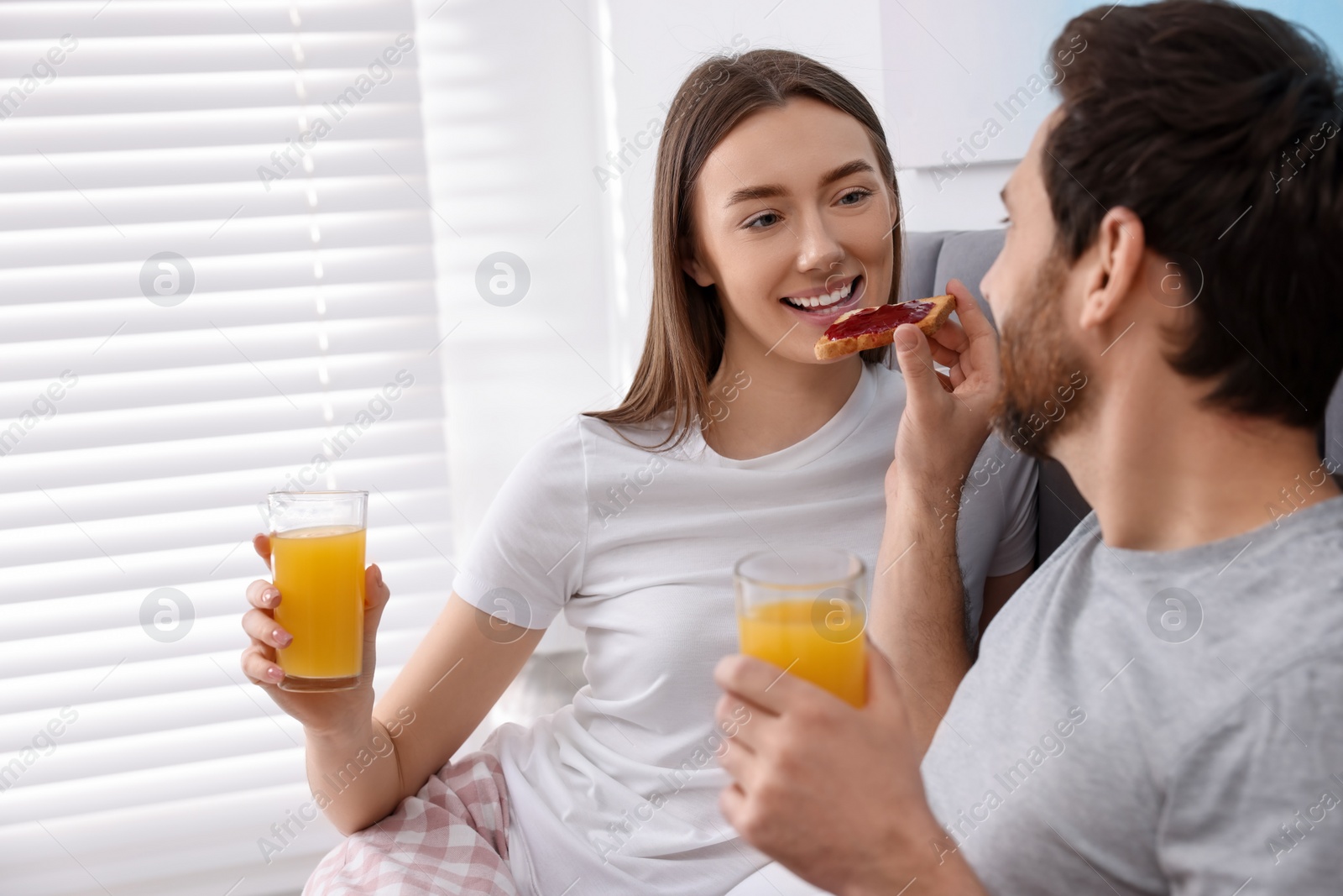 Photo of Tasty breakfast. Husband feeding his wife in bedroom