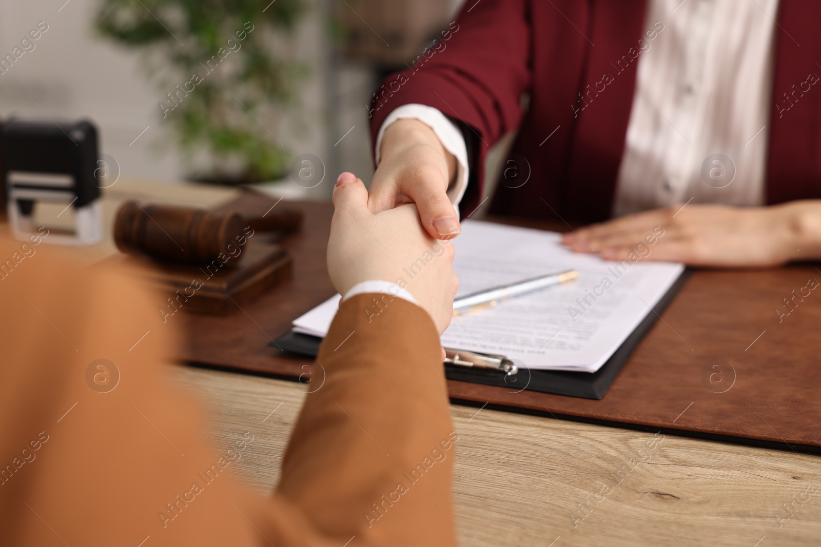 Photo of Notary shaking hands with client at wooden table in office, closeup