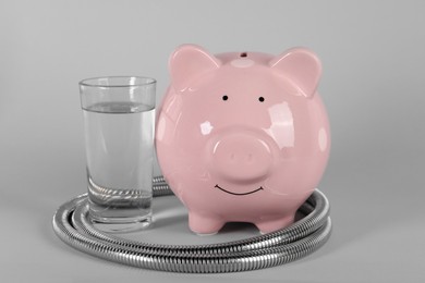 Photo of Water scarcity concept. Piggy bank, shower hose and glass of drink on grey background