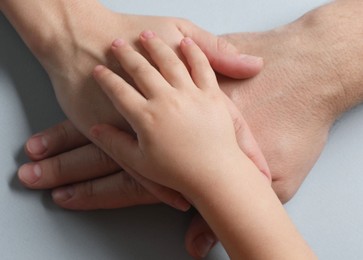Parents and child holding hands together on gray background, top view