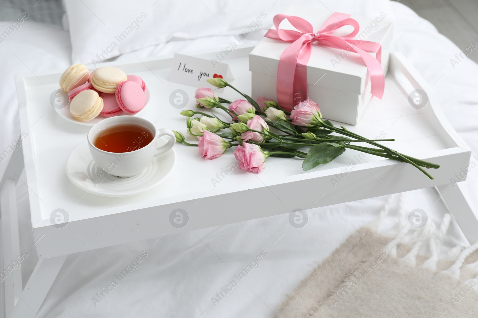 Photo of Tasty breakfast served in bed. Delicious macarons, tea, gift box, flowers and I Love You card on tray