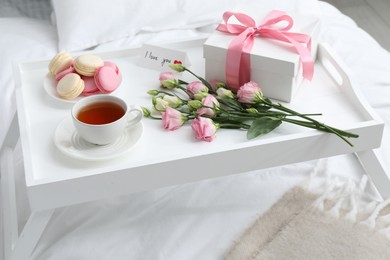 Photo of Tasty breakfast served in bed. Delicious macarons, tea, gift box, flowers and I Love You card on tray