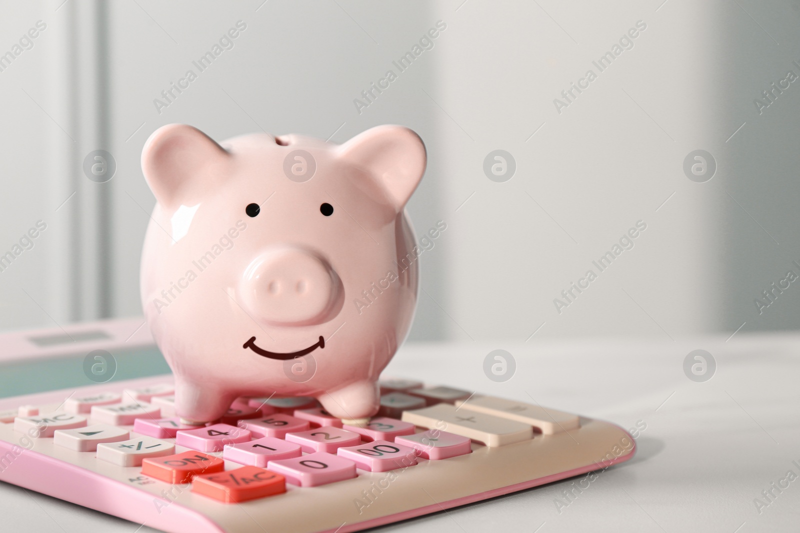 Photo of Ceramic piggy bank and calculator on white marble table, closeup. Space for text