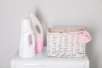 Photo of Baby clothes in wicker basket and laundry detergents on washing machine near light wall