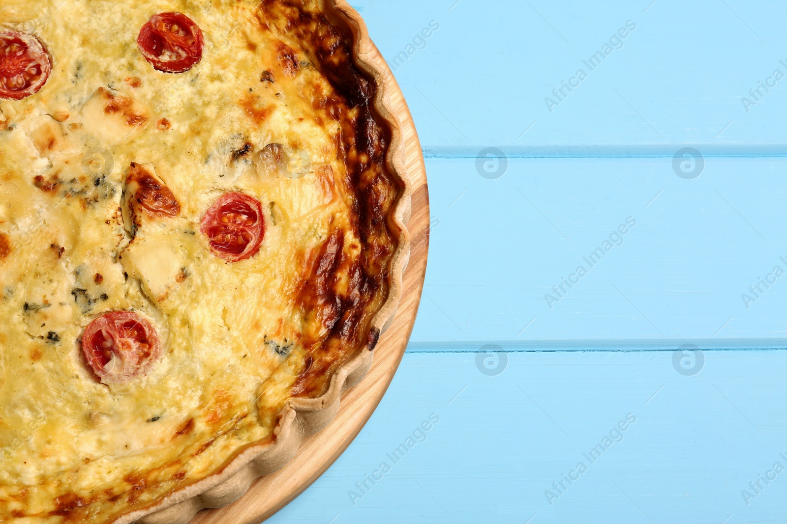 Photo of Delicious quiche with cheese and tomatoes on light blue wooden table, top view. Space for text