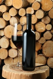 Stylish presentation of red wine in bottle and wineglass near wooden logs