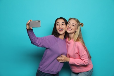 Photo of Young women laughing while taking selfie against color background