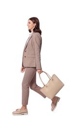 Happy young businesswoman with stylish bag walking on white background