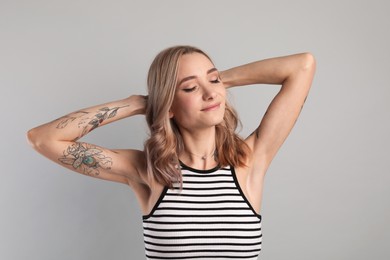 Photo of Beautiful woman with tattoos on arms against grey background