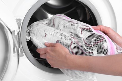 Photo of Woman putting pair of sport shoes in mesh laundry bag into washing machine, closeup