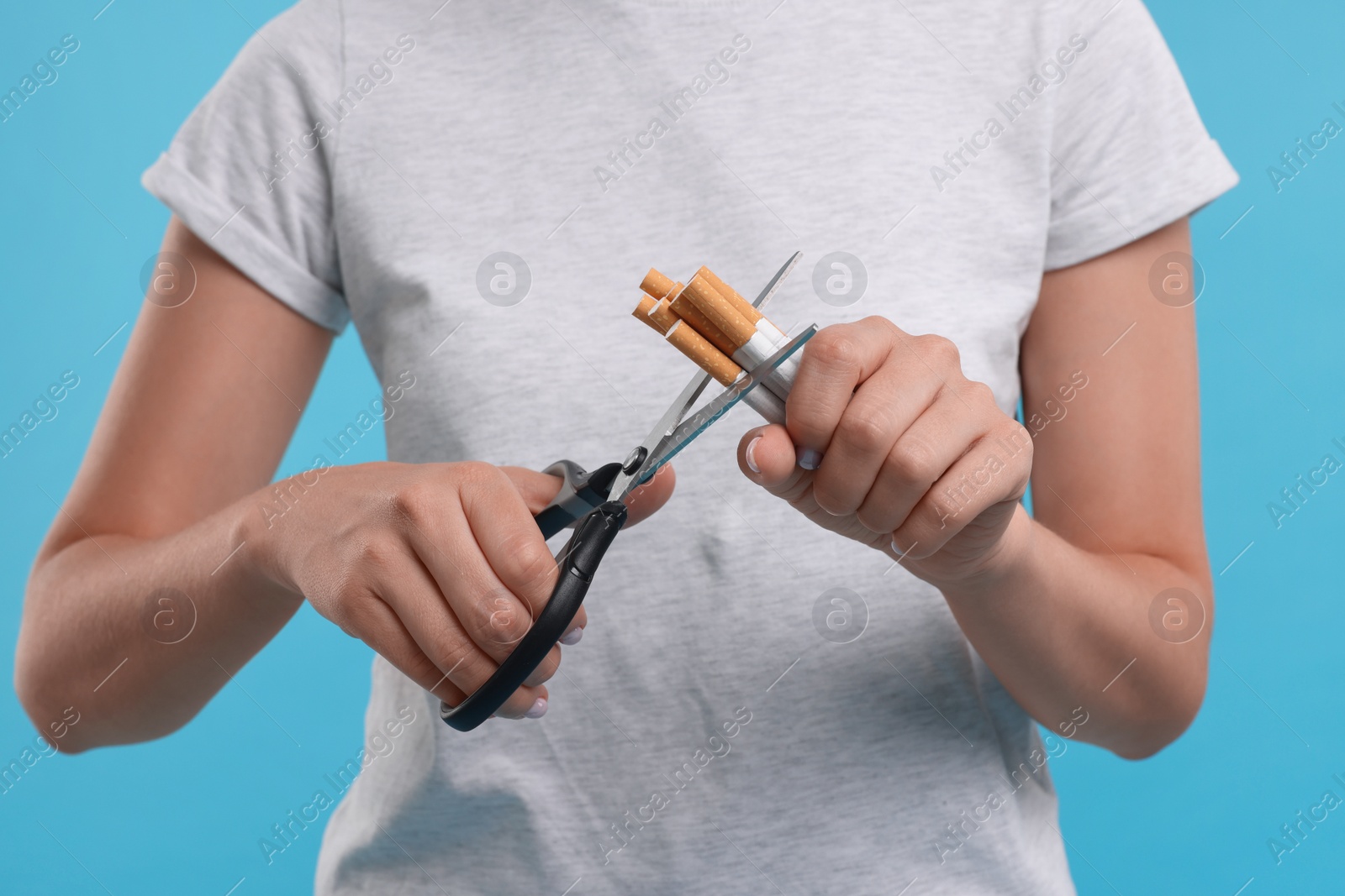 Photo of Stop smoking concept. Woman cutting cigarettes on light blue background, closeup